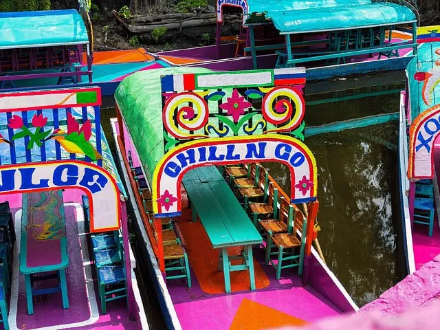 Mehrere leuchtend bunte Trajineras liegen dicht an dicht an einem Kanal vertäut.