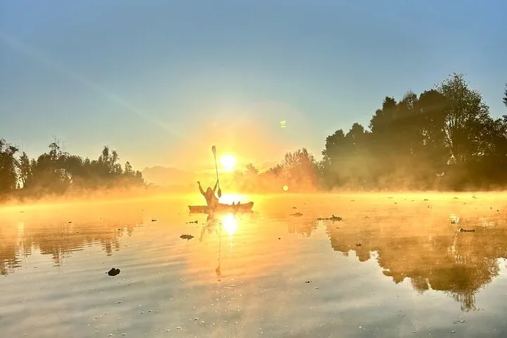 Eine Person beim Kajakfahren auf einem ruhigen Kanal während eines wunderschönen goldenen Sonnenaufgangs.
